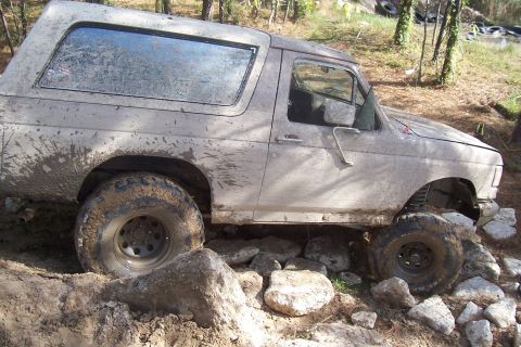 1987 Ford Bronco - This SUV is navigating a rocky, off-road trail, with mud splattered all over its body.