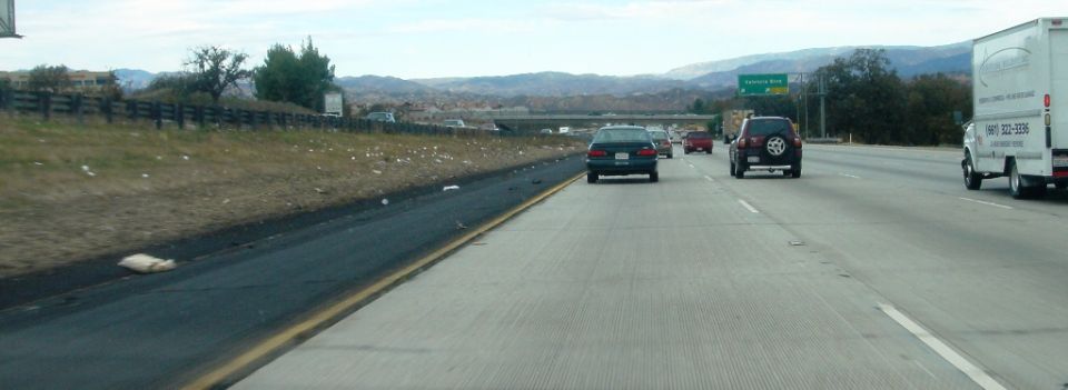 View from a moving car of a multi-lane highway with traffic and dry hills under a hazy sky