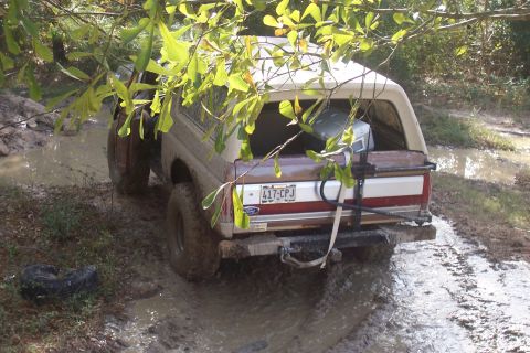 1987 Ford Bronco - This 1987 Ford Bronco is stuck in a muddy off-road trail, with a spare tire lying in the mud beside it.