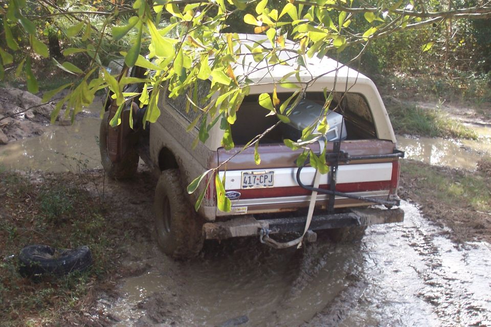 1987 Ford Bronco stuck in mud, rear view. Spare tire on the ground nearby