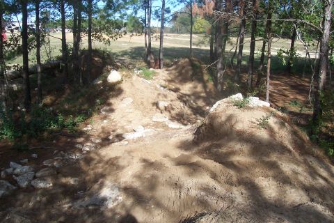 1987 Ford Bronco - A dirt track winds through a wooded area, with the Supermotors.net logo visible in the lower right corner.