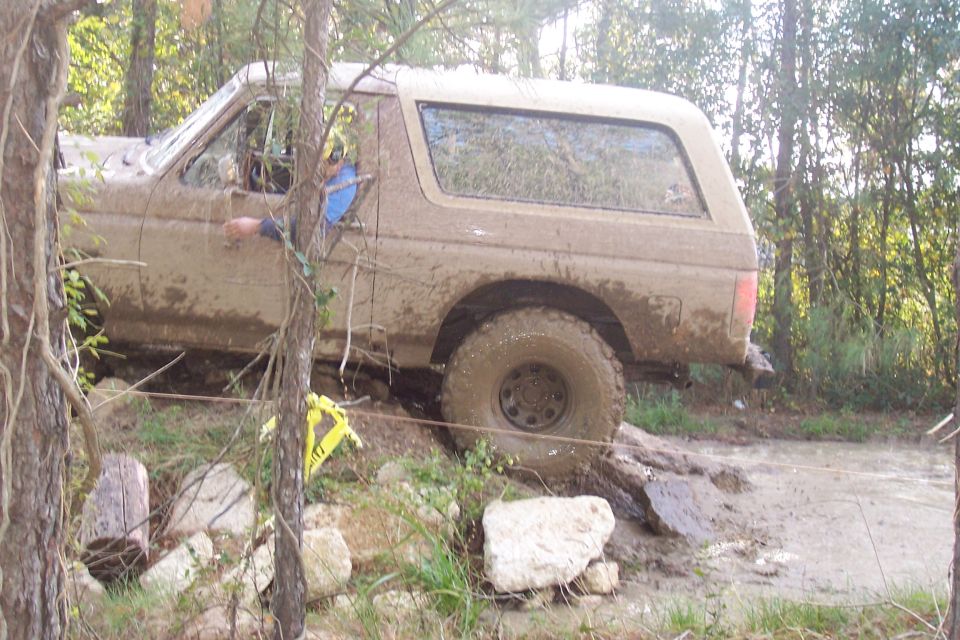 Muddy SUV driving through rough terrain with trees and rocks