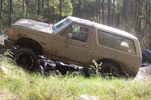 1987 Ford Bronco - 1987 Ford Bronco tackling an off-road trail with mud and rocks.