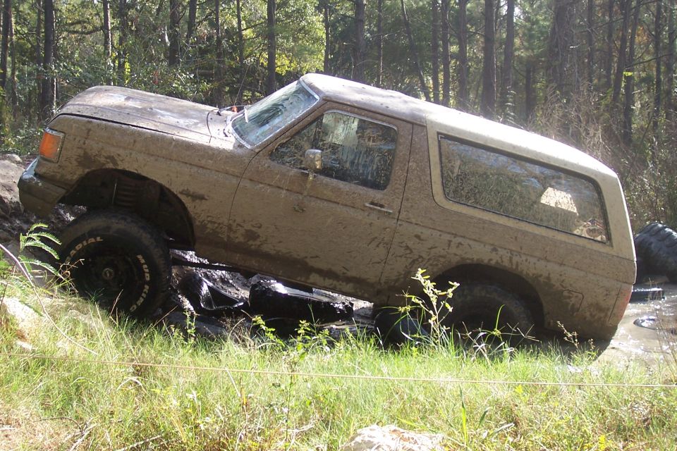 Mud-covered 1987 Ford Bronco navigating rocky terrain