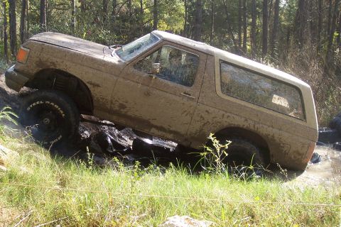 1987 Ford Bronco - This Ford Bronco is navigating a challenging off-road course, covered in mud.