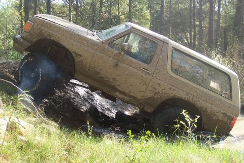 1987 Ford Bronco - A muddy 1987 Ford Bronco navigates an obstacle course in a wooded area.