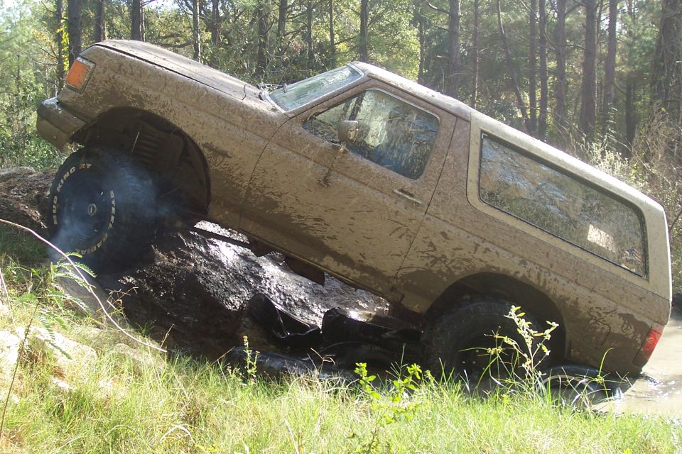 Mud-covered 1987 Ford Bronco on its side on a log, front wheel off the ground