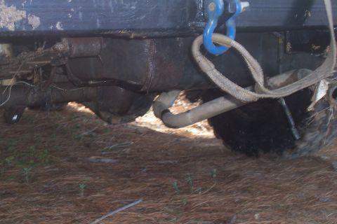 1987 Ford Bronco - A tow strap is attached to a vehicle's frame, near the rear axle and exhaust system.