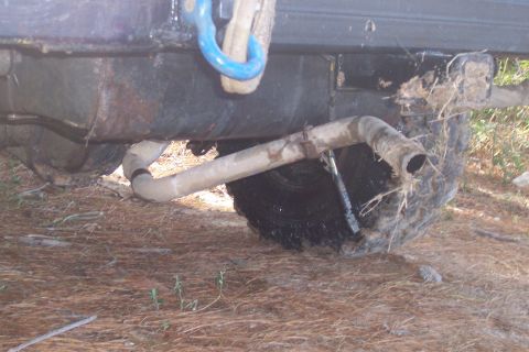 1987 Ford Bronco - The rear of a muddy vehicle shows its exhaust pipe and axle, with a blue tow hook mounted on the frame.