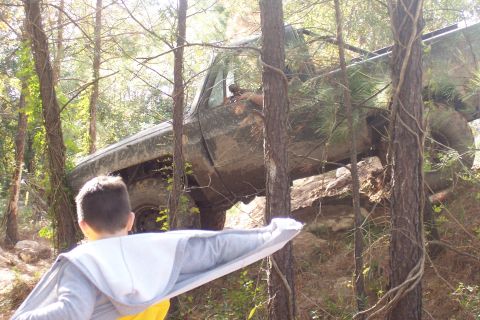 1987 Ford Bronco - A child watches a muddy truck navigate a steep, wooded terrain.
