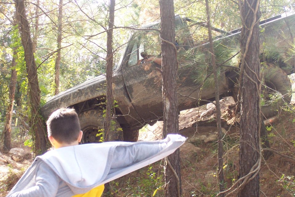 Mud-covered truck on rocky incline, seen from behind a child