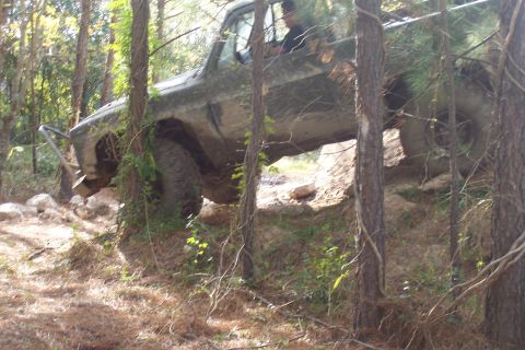 1987 Ford Bronco - This off-road truck navigates a challenging dirt incline amidst a wooded area.