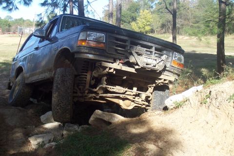 1987 Ford Bronco - This black Ford Bronco is shown off-roading over rocks and dirt, demonstrating its capabilities.