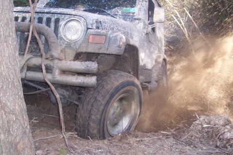 1987 Ford Bronco - A Jeep Wrangler navigates a muddy trail, with its tires churning up dirt and debris.
