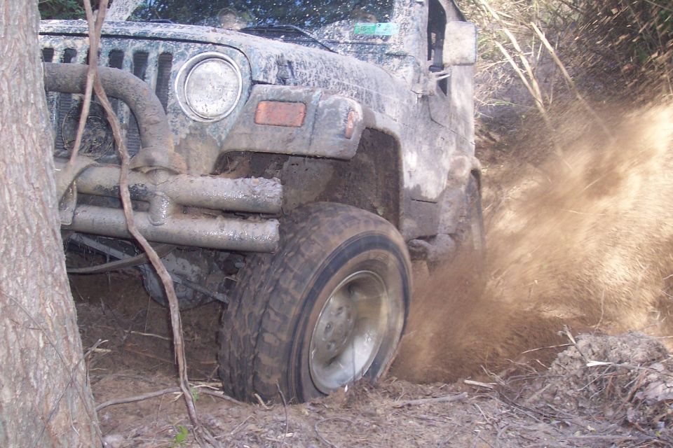 Muddy Jeep Wrangler driving through dirt and brush. Front tire is kicking up a lot of mud