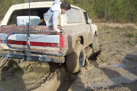 1987 Ford Bronco - This 1980s Ford Bronco is deeply stuck in the mud, with a child partially visible in the cargo area.