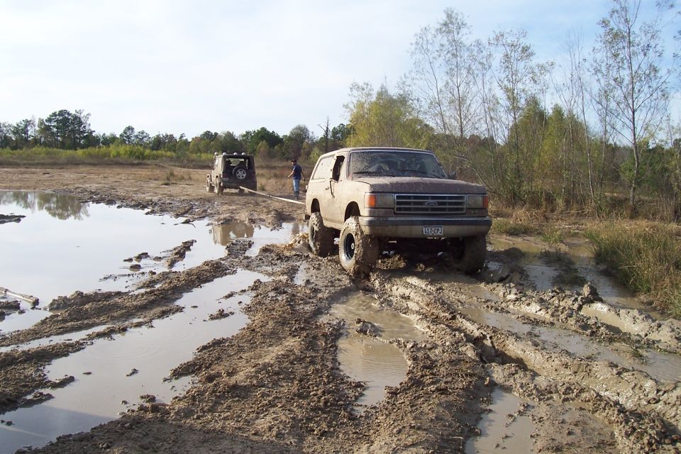 1987 Ford Bronco being towed through mud by a Jeep