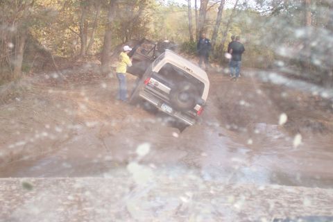 1987 Ford Bronco - A 1987 Ford Bronco is stuck in a muddy off-road trail with several people observing.