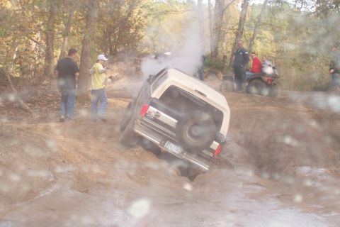 1987 Ford Bronco - A 1987 Ford Bronco navigates a muddy off-road course with onlookers nearby.