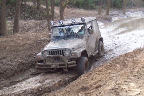 1987 Ford Bronco - A Jeep Wrangler TJ navigates a muddy trail, its front tires deep in the muck.