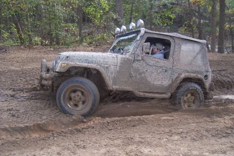 1987 Ford Bronco - A driver navigates a heavily muddied off-road path in a Jeep Wrangler.