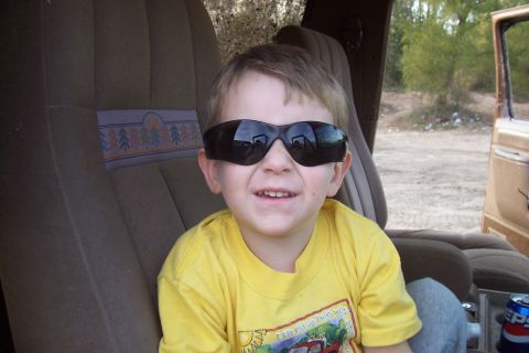 1987 Ford Bronco - A young boy with sunglasses on smiles while sitting in the passenger seat of a vehicle.