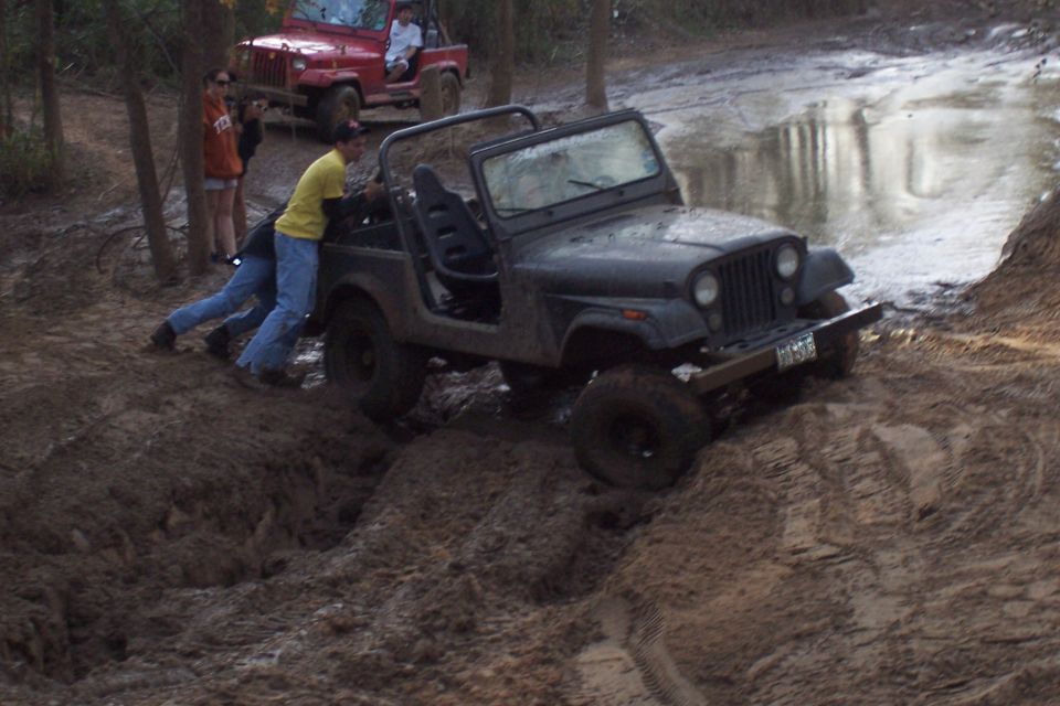 Black Jeep CJ-7 stuck in mud, people pushing. Red Jeep in background
