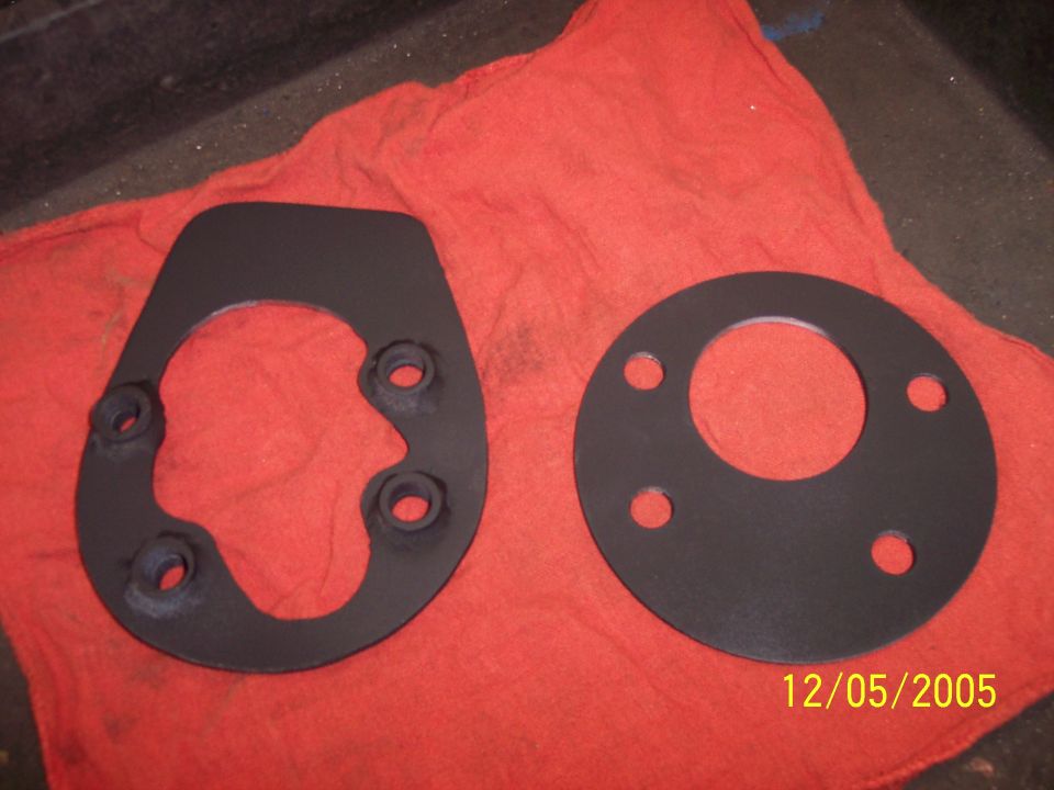 Two black mounting plates with bolt holes resting on a red cloth