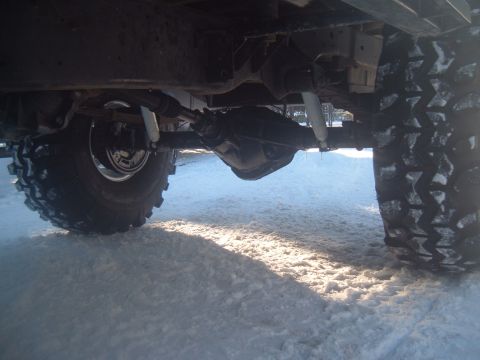 1989 Ford Bronco - The underside of a vehicle, showing the drivetrain and large tires, is visible in a snowy environment.