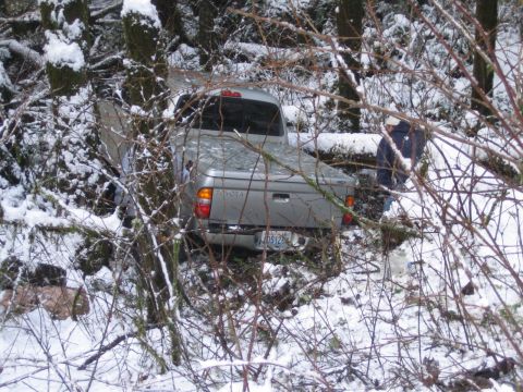 1990 Ford Bronco - A silver Toyota pickup truck is stuck off-road in a snowy, wooded area.