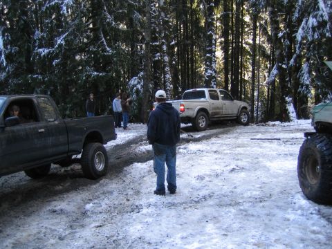 1990 Ford Bronco - Multiple trucks are parked on a snowy road in a wooded area.