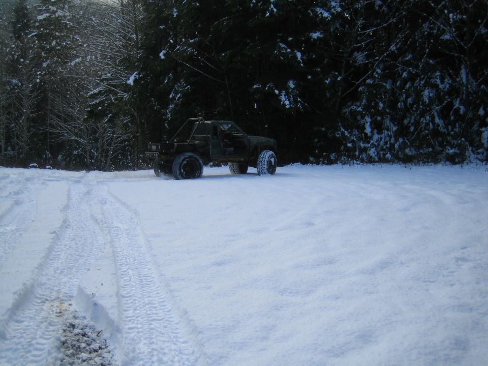 Off-road vehicle with roll cage parked in a snowy area with trees in the background