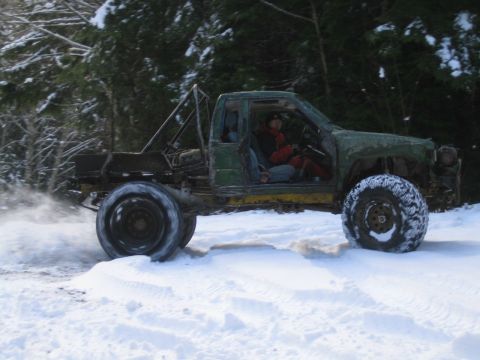 1990 Ford Bronco - A heavily modified green truck with a roll cage navigates a snowy terrain with a driver inside.