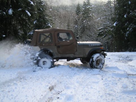1990 Ford Bronco - Jeep CJ-7 Laredo with soft top driving through snow, kicking up spray.