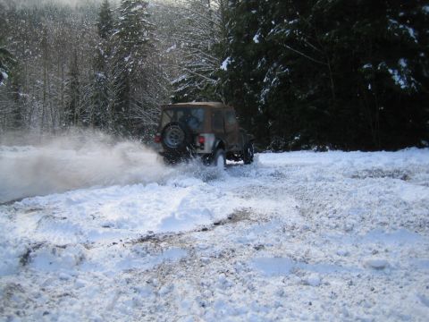 1990 Ford Bronco - A Jeep CJ-7 navigates a snowy path, spraying snow as it turns.