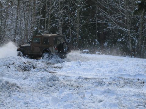 1990 Ford Bronco - A Jeep Wrangler navigates a snowy trail, its tires churning through the deep snow.