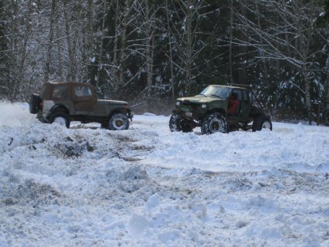 1990 Ford Bronco - Two off-road vehicles navigate a snowy landscape with trees in the background.