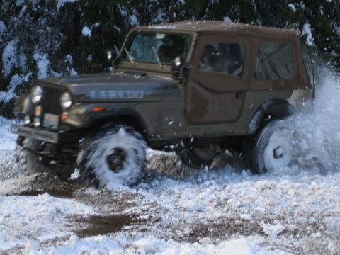 1990 Ford Bronco - A Jeep CJ-7 Laredo kicks up snow as it drives through a wintery landscape.
