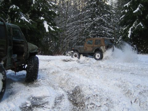1990 Ford Bronco - Off-road vehicles navigate a snowy trail, kicking up snow as they go.