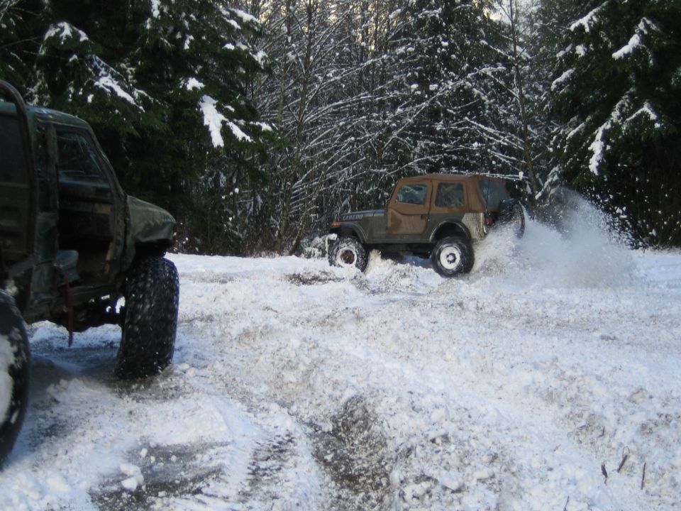 Two off-road vehicles driving through deep snow in a wooded area