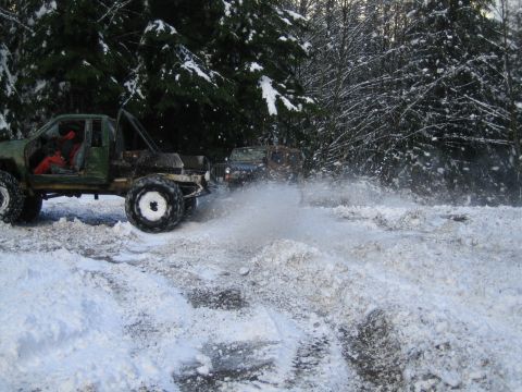 1990 Ford Bronco - Off-road vehicles navigate a snowy path, spraying water and snow.
