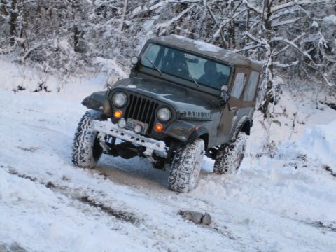 1990 Ford Bronco - A Jeep CJ-7 Laredo navigates a snowy trail, its tires kicking up snow as it drives through the winter landscape.
