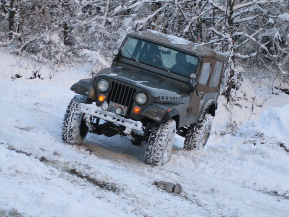 Dark green Jeep CJ-7 Laredo with soft top driving in snow