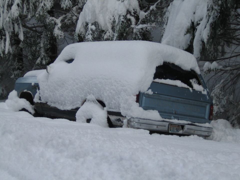 Blue SUV buried in snow, only rear bumper and taillights visible. License plate reads 611-NBP