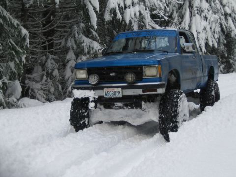 1990 Ford Bronco - A blue pickup truck navigates a snow-covered path, its large tires digging into the snow.