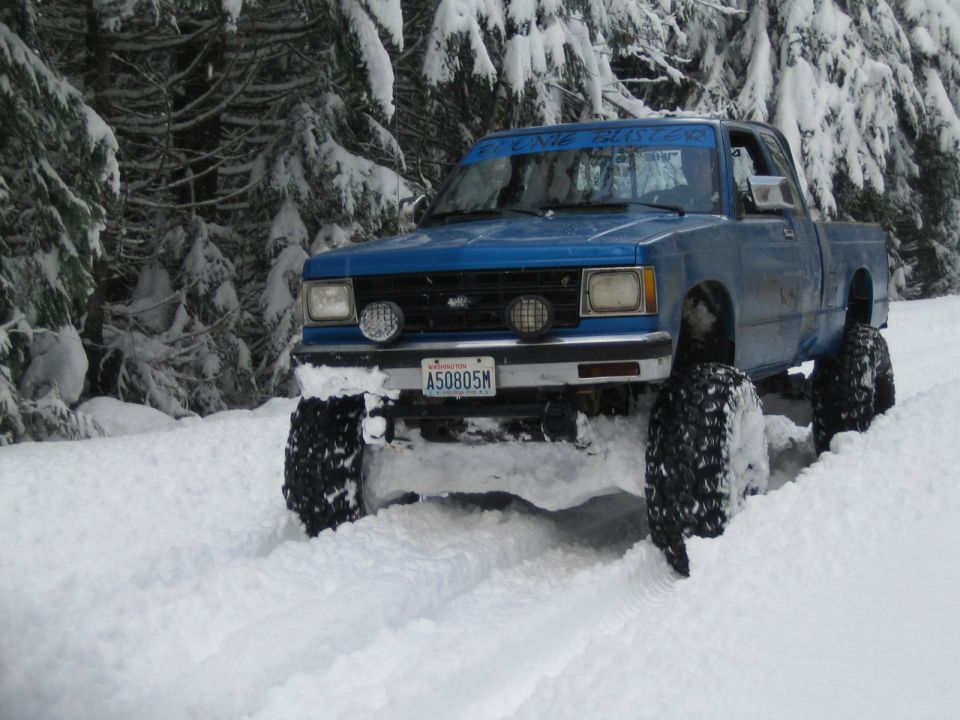 Blue pickup truck with oversized tires driving through deep snow