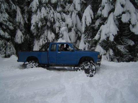 1990 Ford Bronco - A blue pickup truck navigates a snowy landscape, with snow-laden trees forming a backdrop.