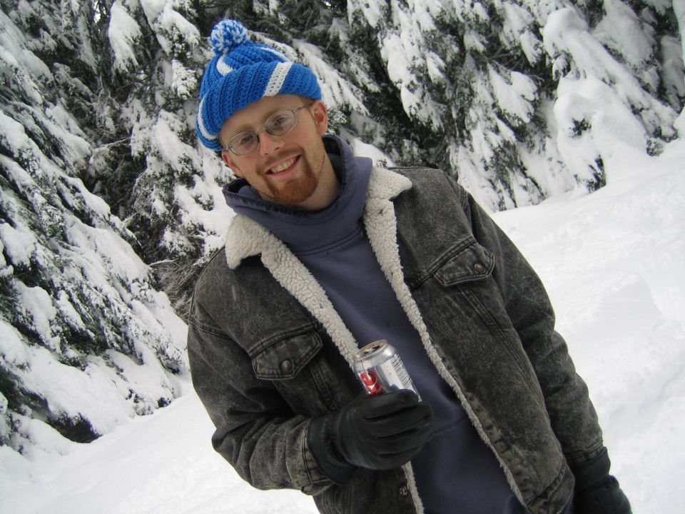 Man in blue hat and denim jacket holding a can in snowy woods
