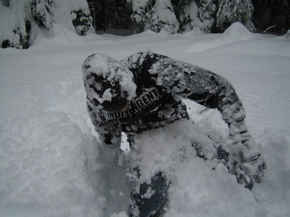 Person buried in snow, wearing a black jacket with white text