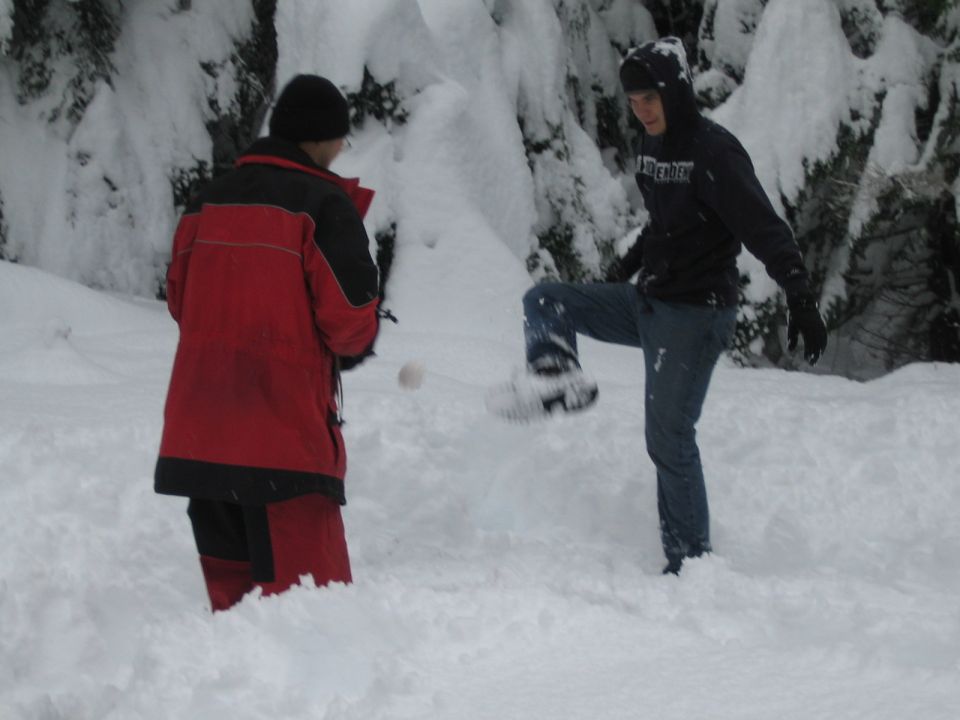 Two people in a snowy forest scene, one wearing a red jacket, the other in a black hoodie